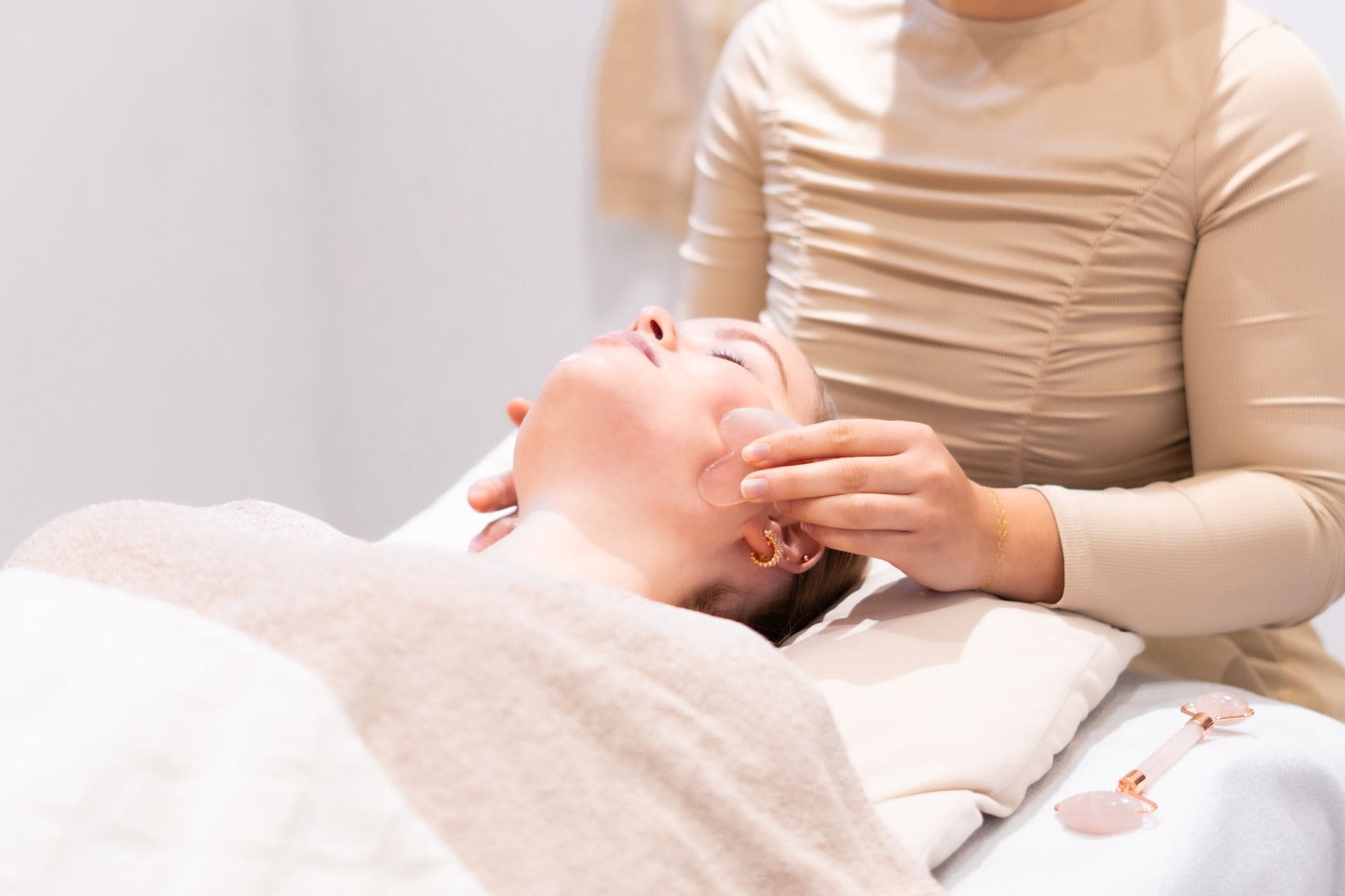 Een vrouw krijgt een gezichtsbehandeling met een gua sha steen op de behandeltafel.